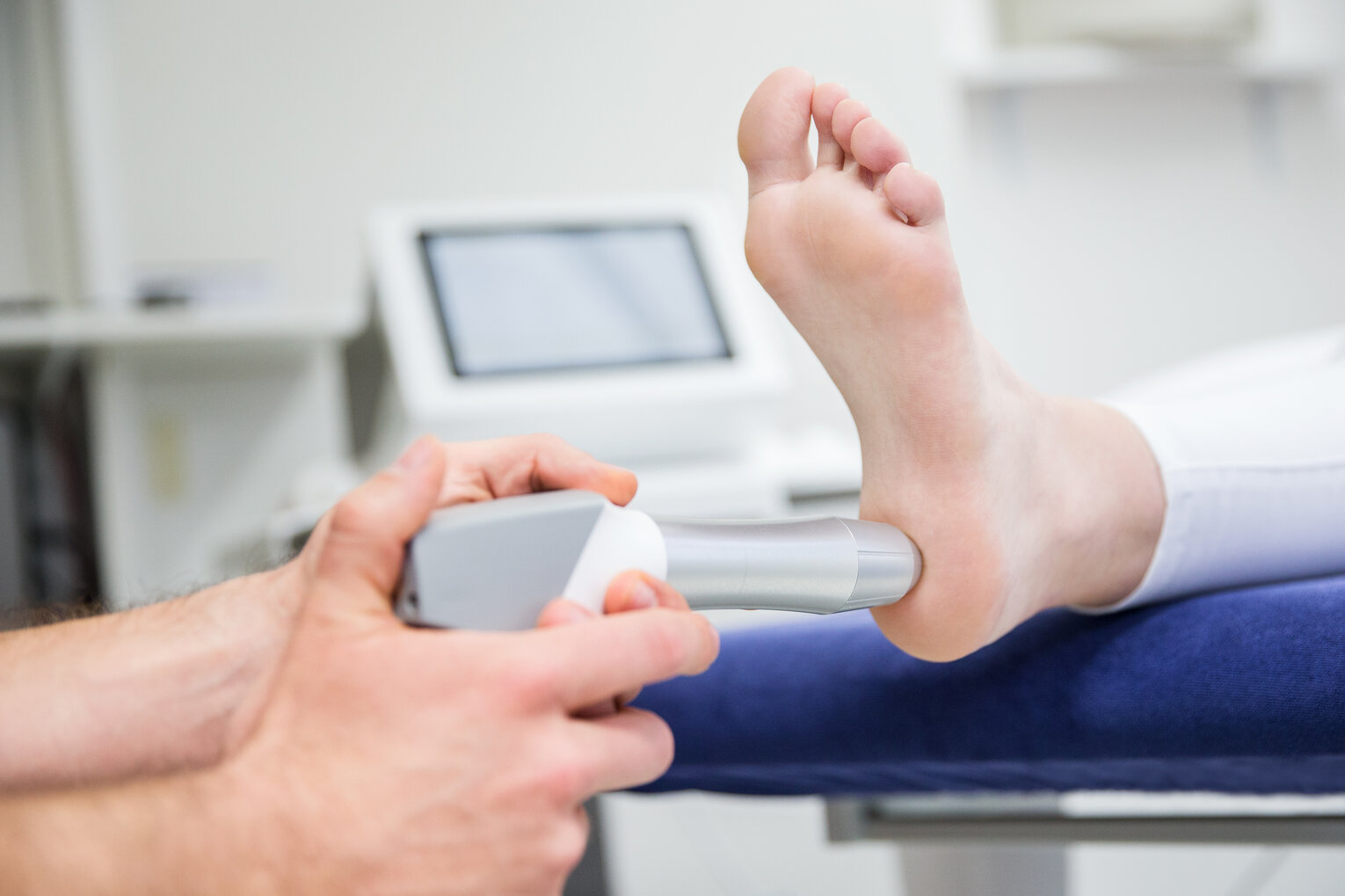 Stoßwellentherapie Eine medizinische Behandlung eines Fußes mit einem Gerät zur Stoßwellentherapie in einer klinischen Umgebung.